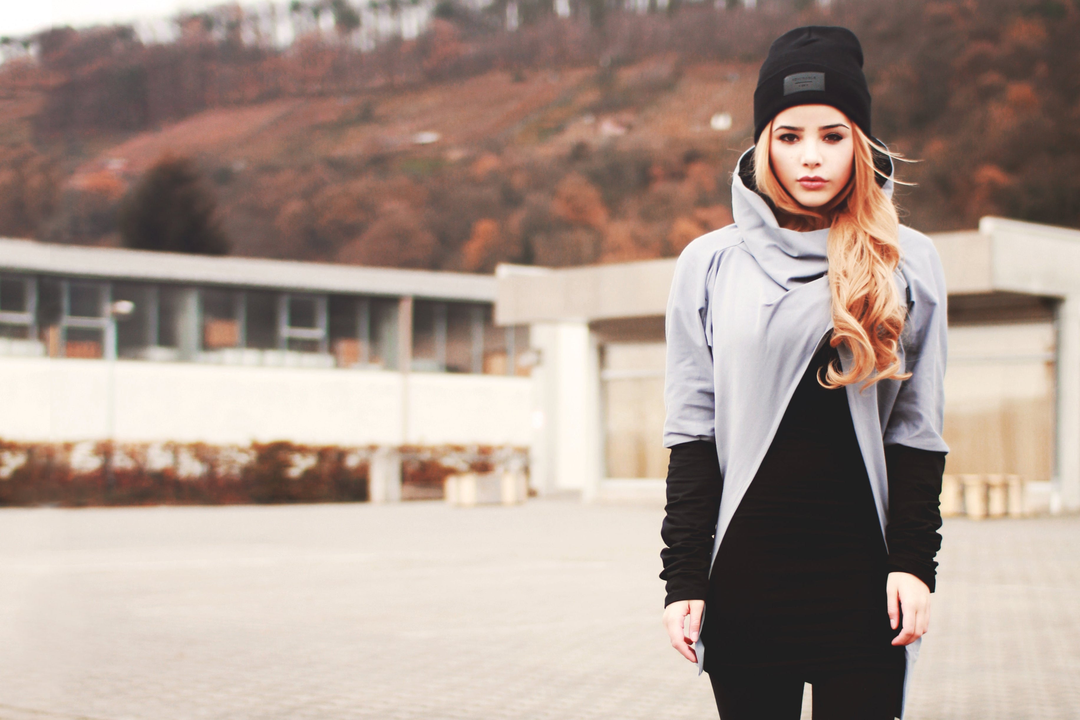 Woman in a gray sweater and black pants standing outdoors with a blurred background